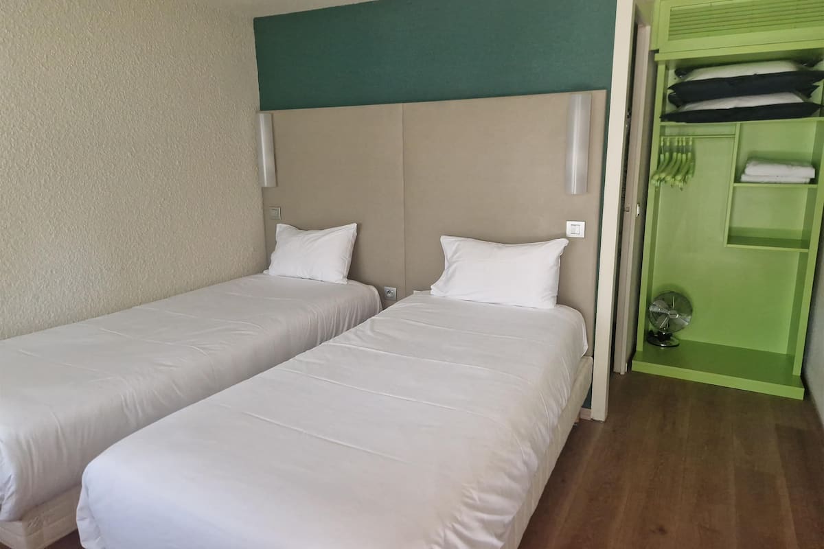 A hotel room with two single beds, a green wardrobe, and a small fan.