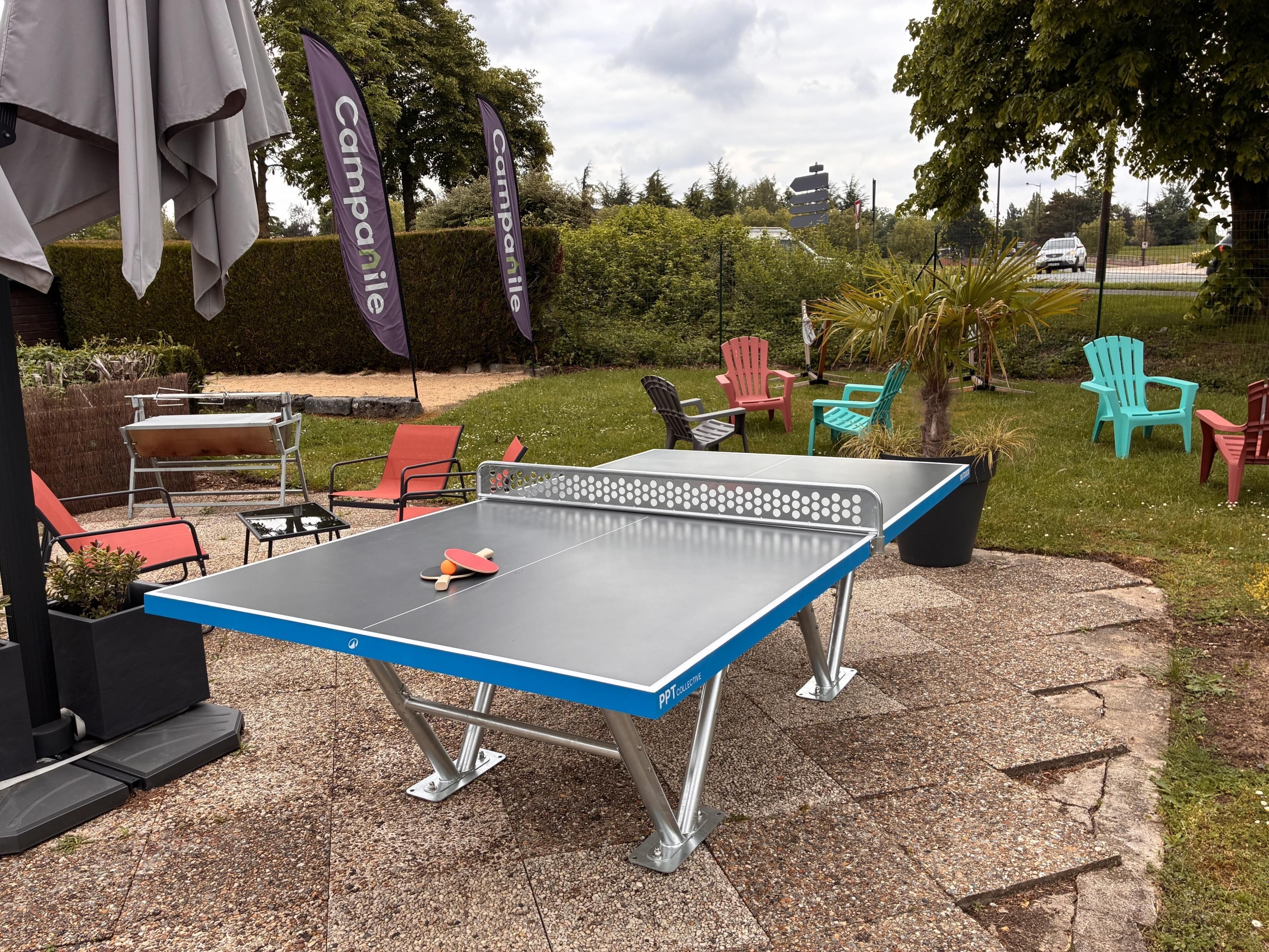 Mesa de ping pong al aire libre con sillas y una raqueta de tenis de mesa.