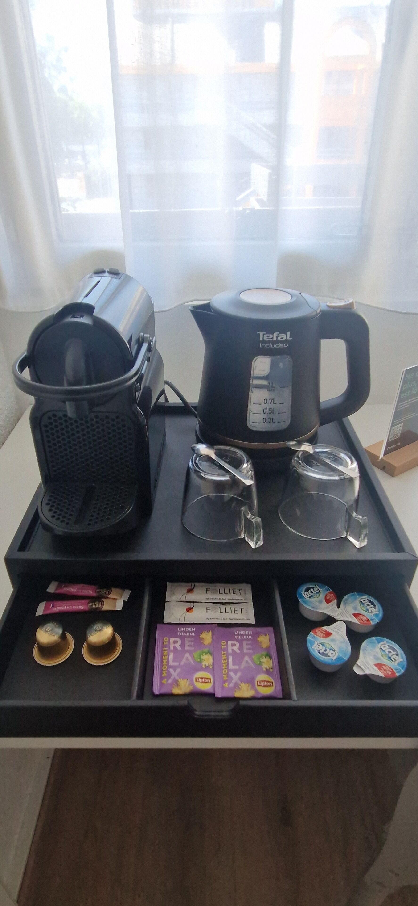 A coffee station with a coffee maker, cups, and Lipton tea packets.
