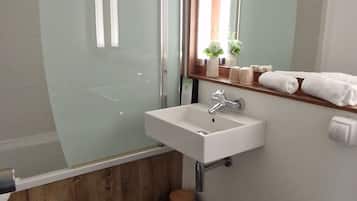 A bathroom with a glass shower enclosure, a white sink, a mirror, a toilet, and a wooden vanity.