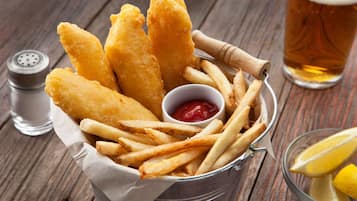 Ein Teller Fish and Chips mit einer kleinen Ketchup-Tüte, einem Bierglas und einem Salzstreuer auf einer Holztischplatte.