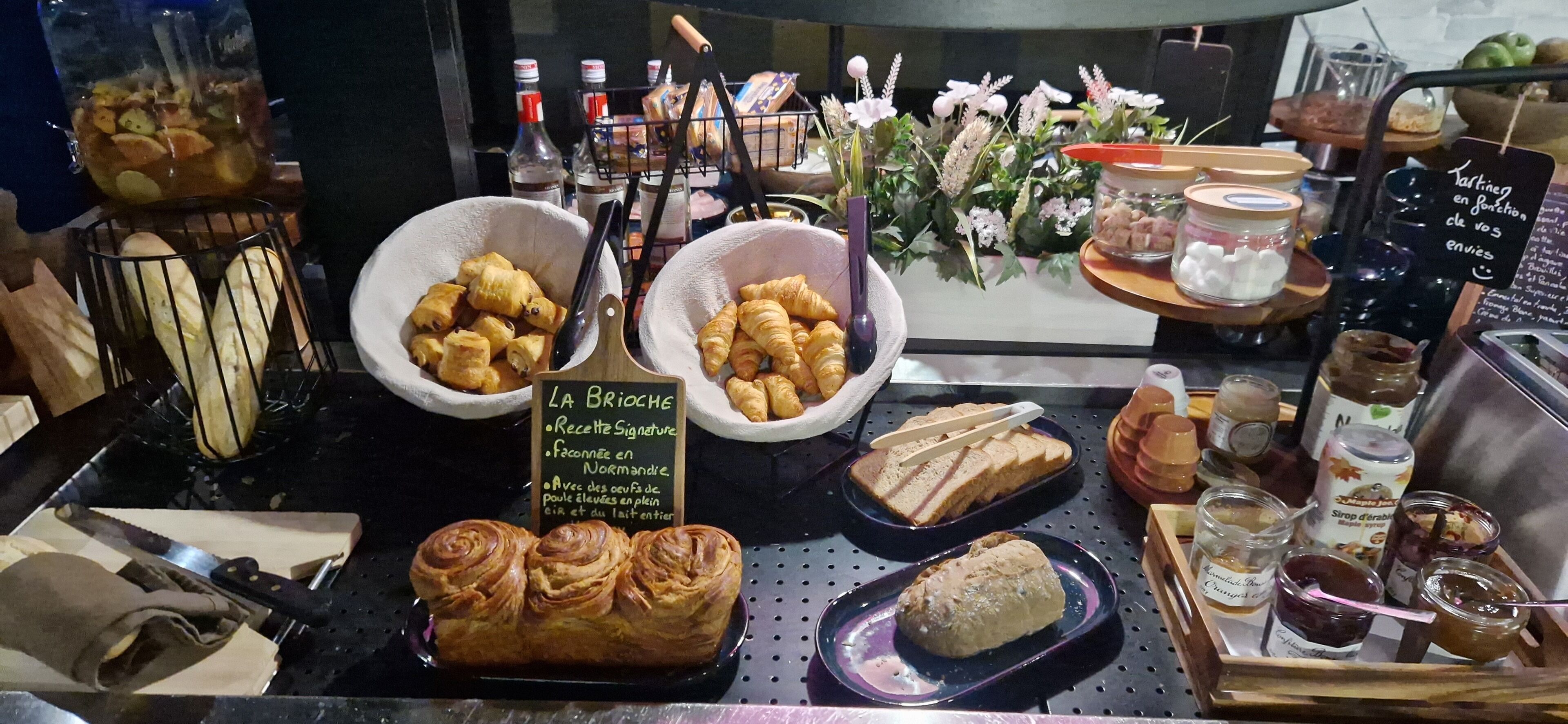 A bakery display with various baked goods and pastries, including croissants and bread, along with jars of spreads and condiments.