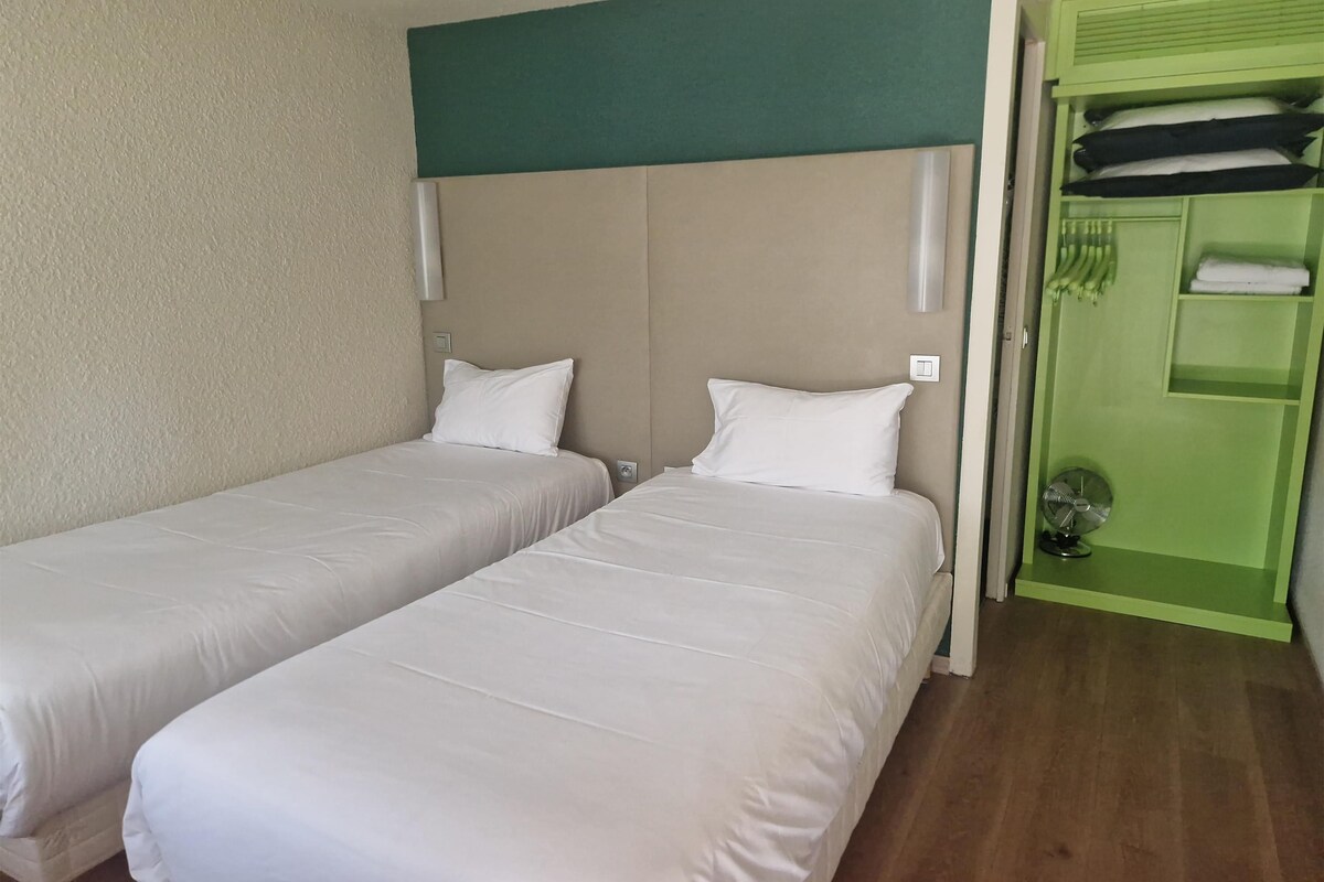 Habitación de hotel con dos camas individuales, un armario verde y un pequeño ventilador.