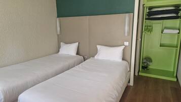 A hotel room with two single beds, a green wardrobe, and a small fan.