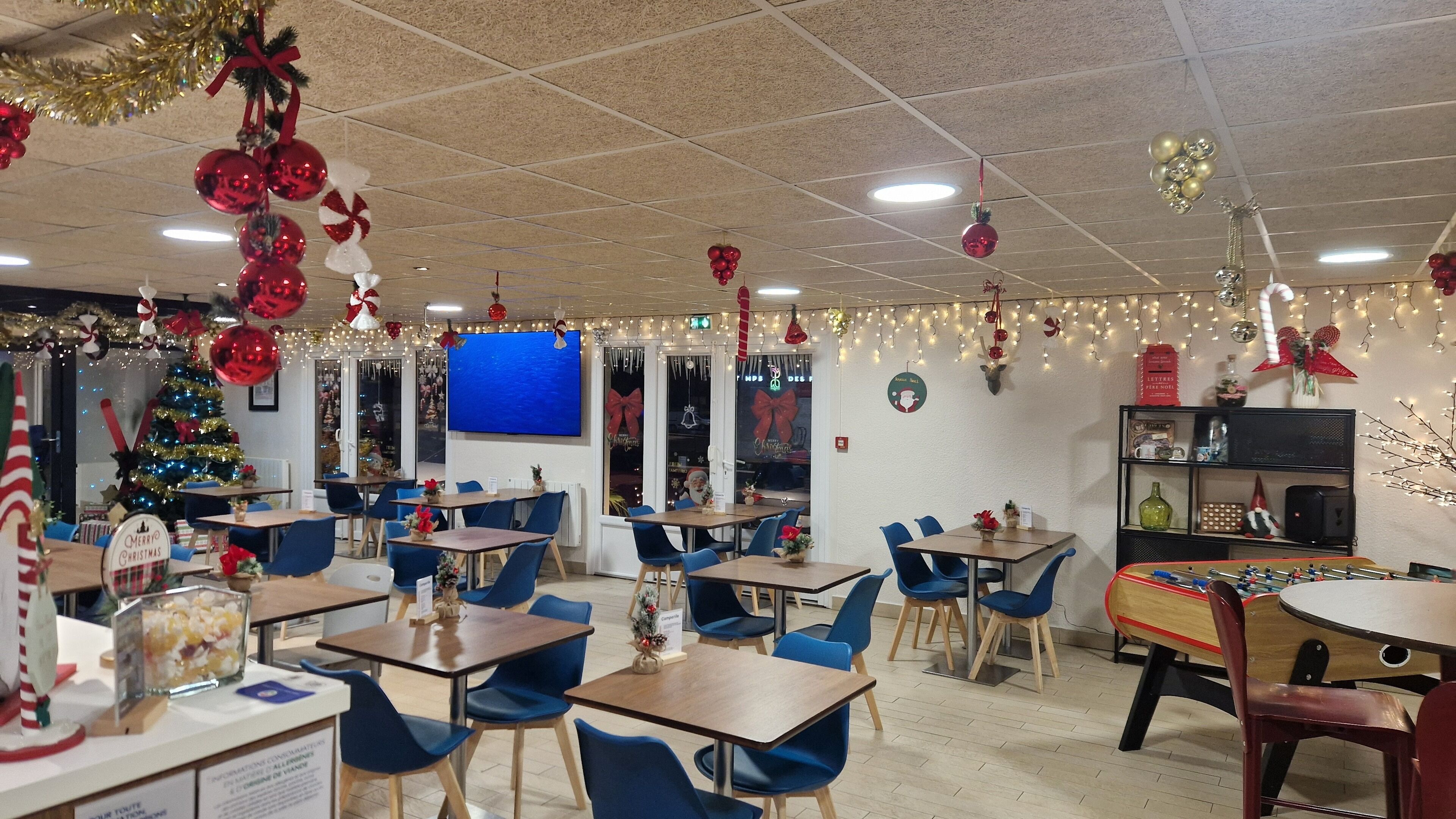 A restaurant with blue chairs and wooden tables, decorated with Christmas ornaments and lights.