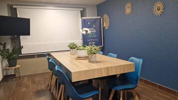 Une salle de conférence avec une table en bois, des chaises bleues, des plantes en pot et une banderole sur laquelle on peut lire : « BIENVENUE ».