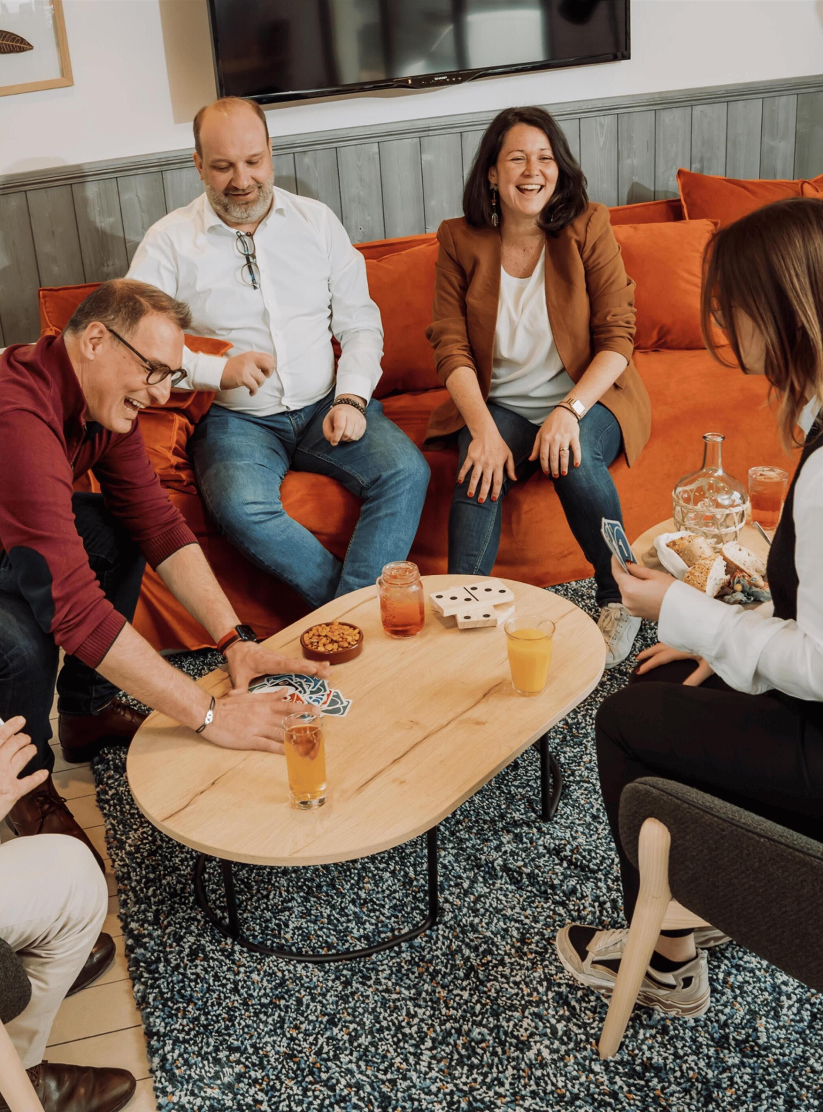 Eine Gruppe von Menschen sitzt auf einer Couch an einem Tisch mit Getränken und Snacks.