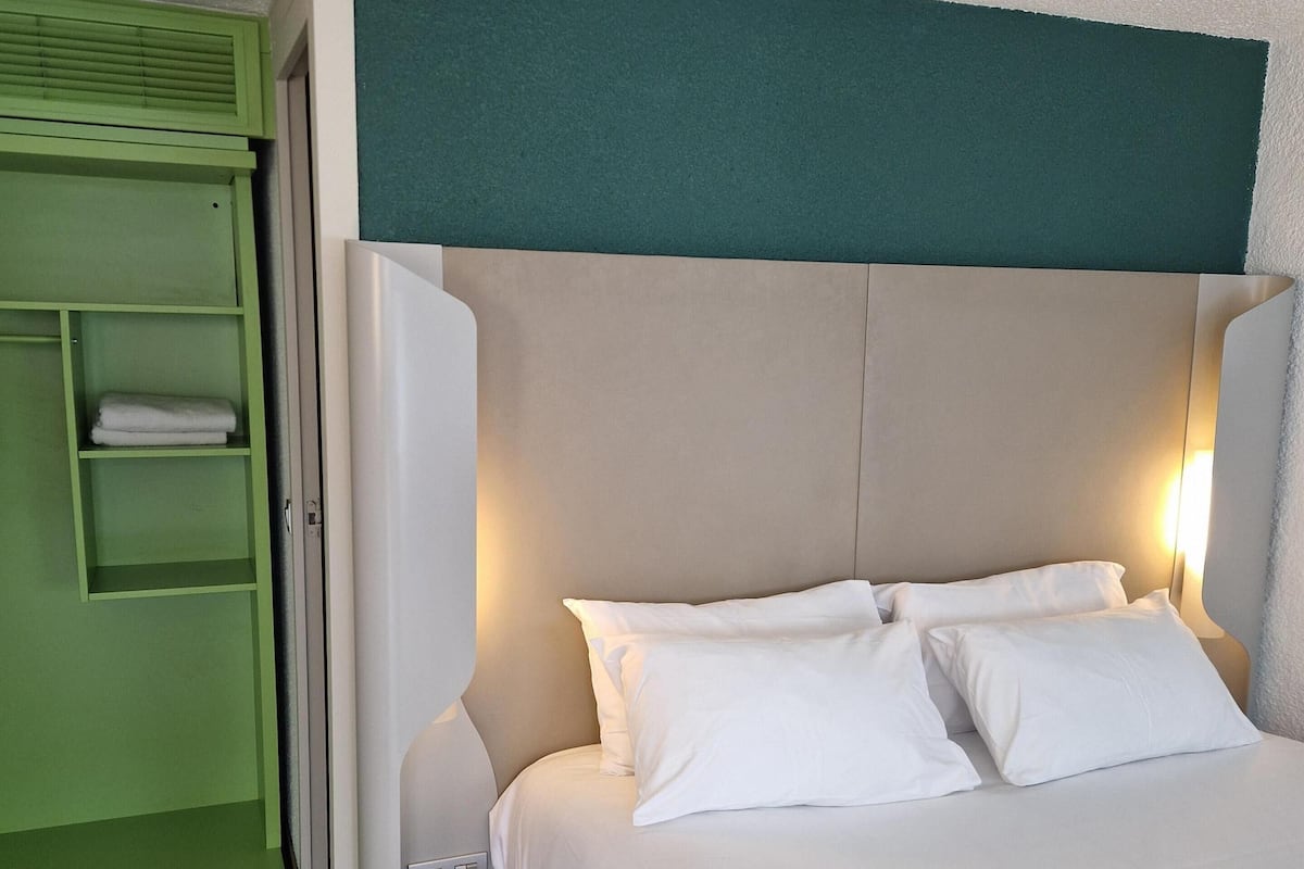 A neatly made bed with white linens and a headboard with a teal accent.