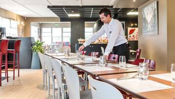 Un restaurant avec de longues tables, des chaises rouges et un chef qui prépare les plats.