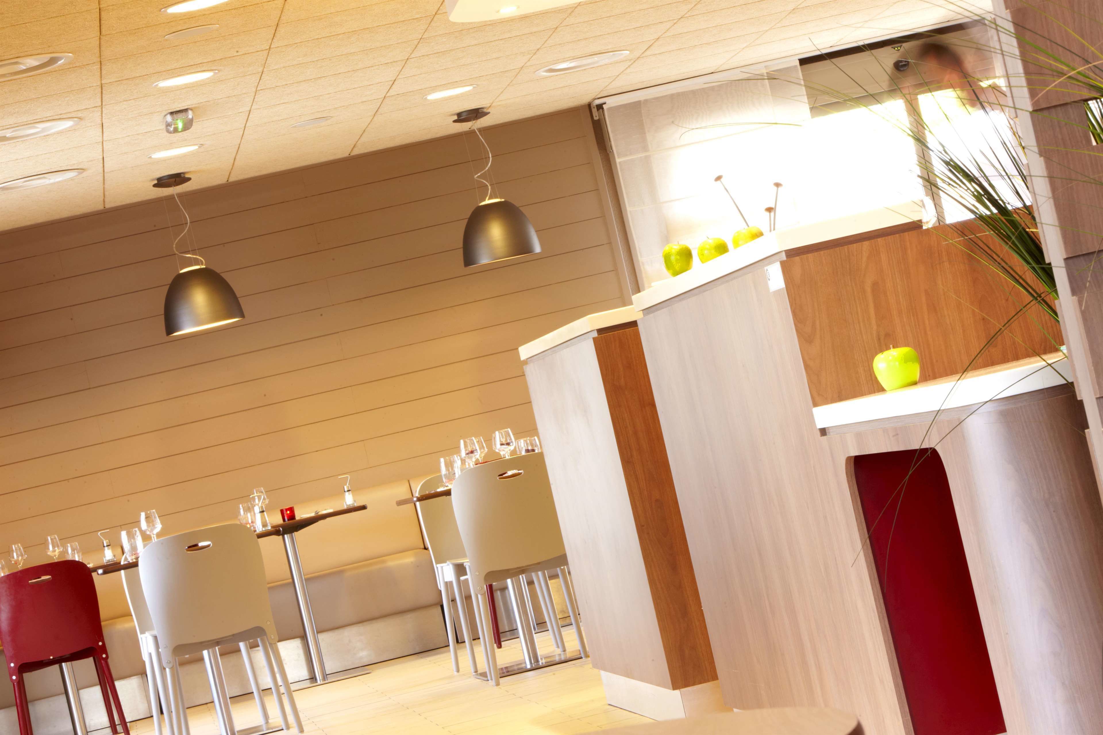 Een modern restaurantinterieur met houten lambrisering, witte en rode stoelen, en hanglampen.
