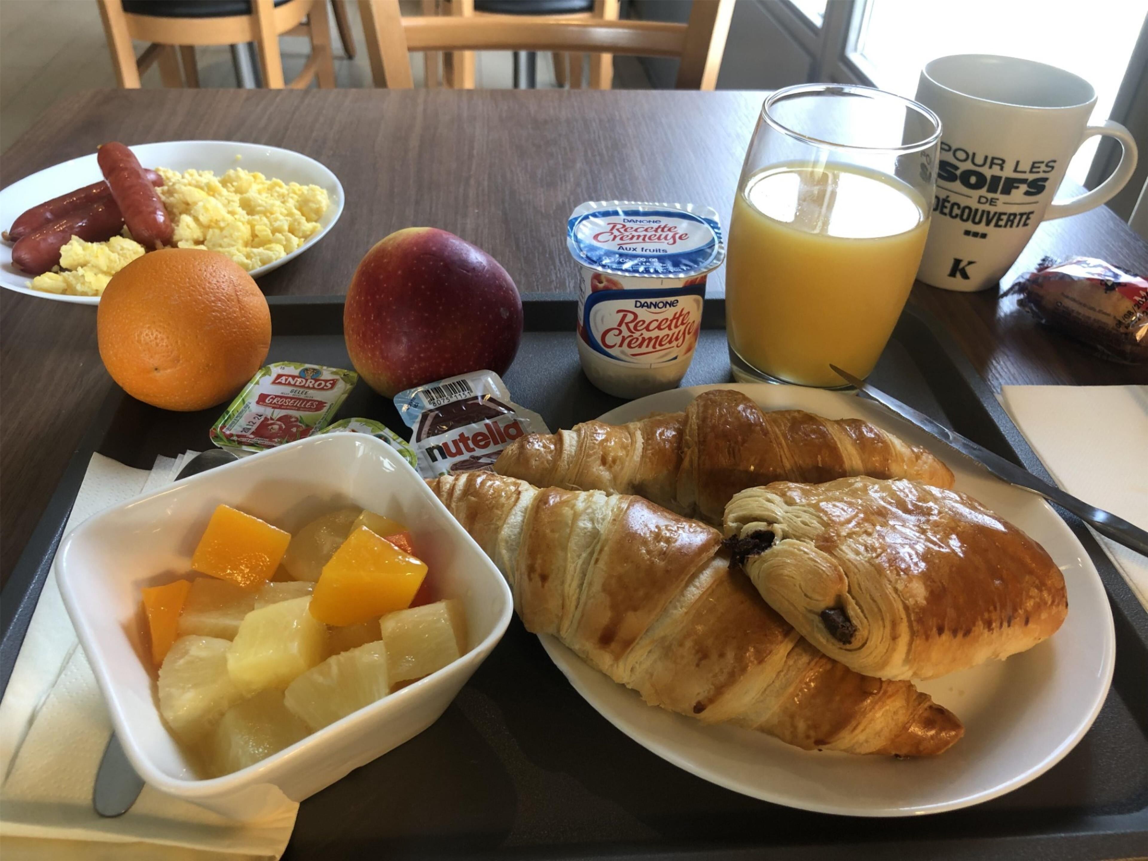 A breakfast table with croissants, fruit, yogurt, and juice.