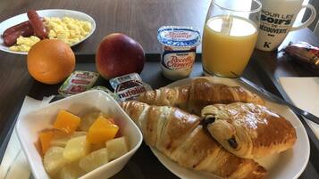 A breakfast table with croissants, fruit, yogurt, and juice.