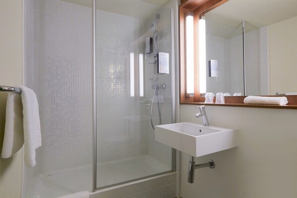 A modern bathroom with a glass-enclosed shower, a white sink, and a mirror above it.