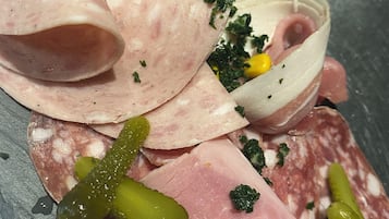 Diverse vleessoorten, zoals plak ham, salami en parmaham, vergezeld van augurken, mais en een kleine schaal groen.