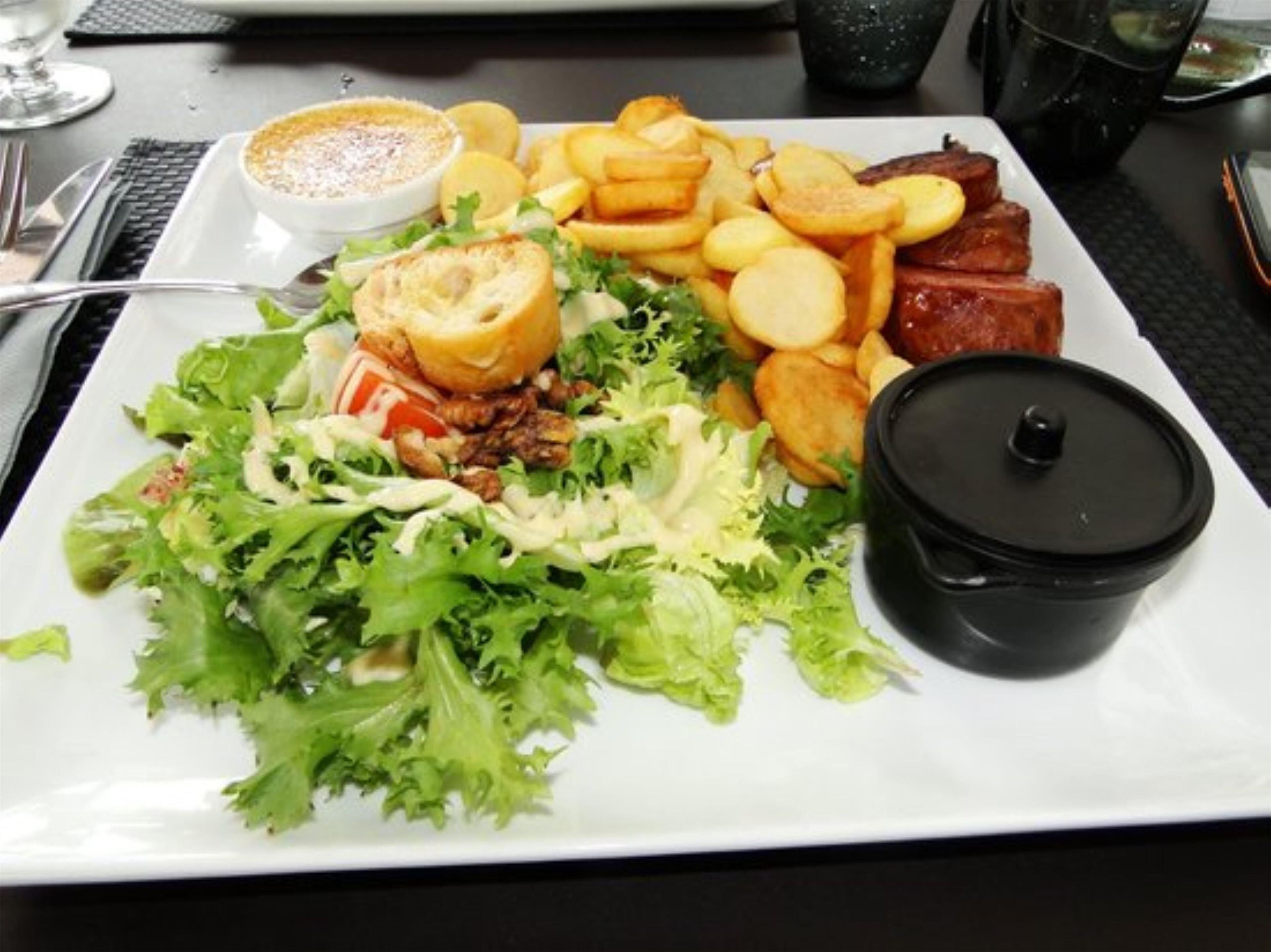 A plate of food with a salad, roasted potatoes, and meat, accompanied by a small bowl of sauce.