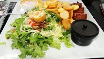 Un plato de comida con ensalada, patatas asadas y carne, acompañado de un recipiente pequeño con salsa.