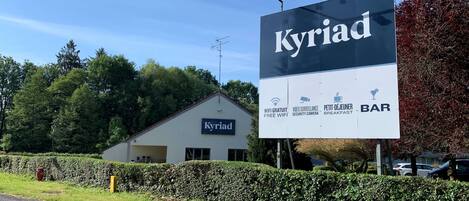 Un edificio con un letrero que dice "Kyriad" y que ofrece acceso a internet WiFi gratuito, una cámara de seguridad, una barra de desayuno y una pequeña cafetería.