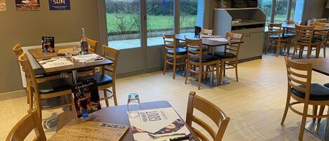 Un restaurante con mesas y sillas de madera, menús y vistas al exterior a través de amplios ventanales.