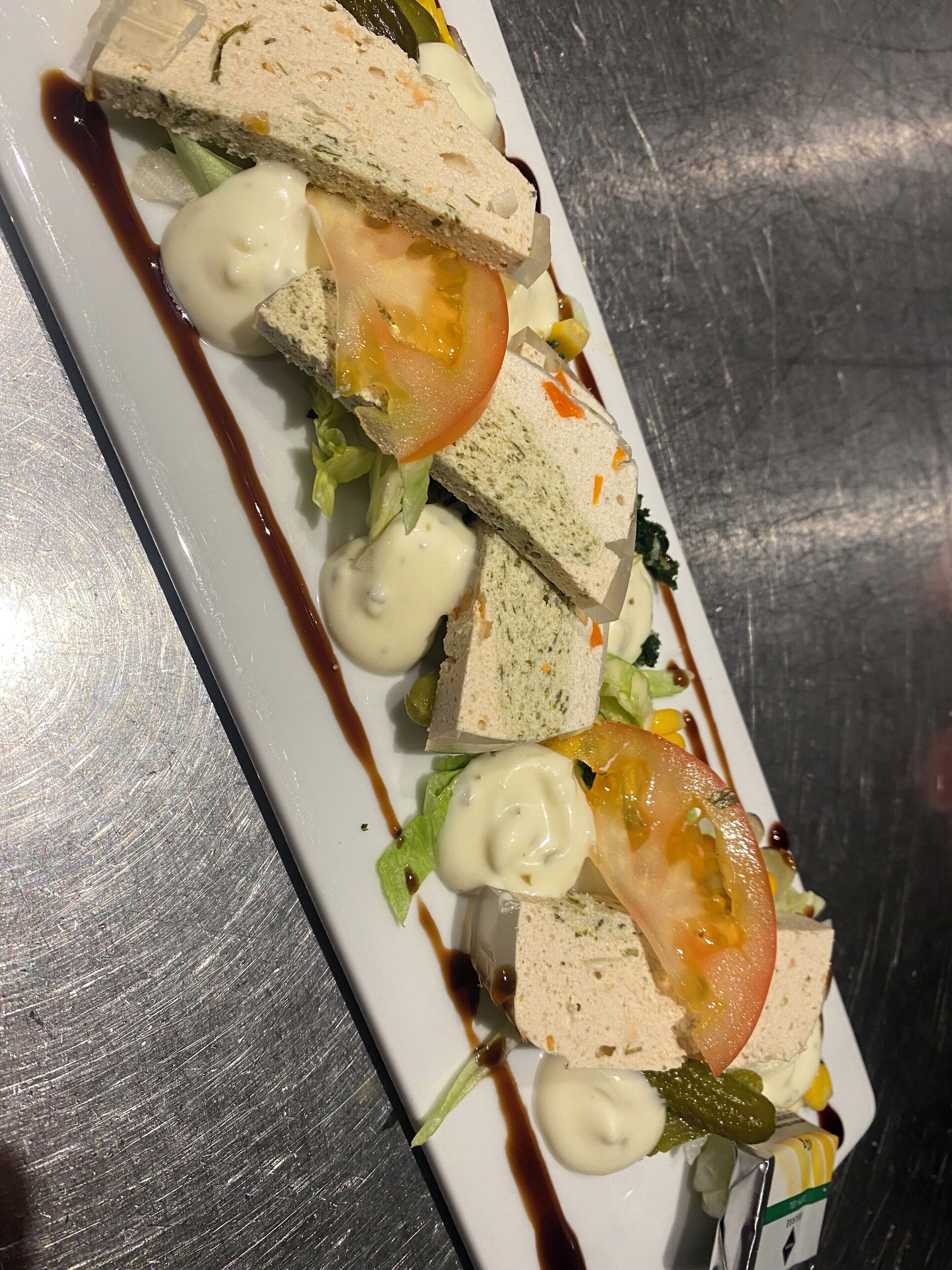 Une assiette rectangulaire blanche sur laquelle est servi un sandwich coupé en deux, garni d’une tranche de tomate, de laitue et d’une cuillerée de sauce.