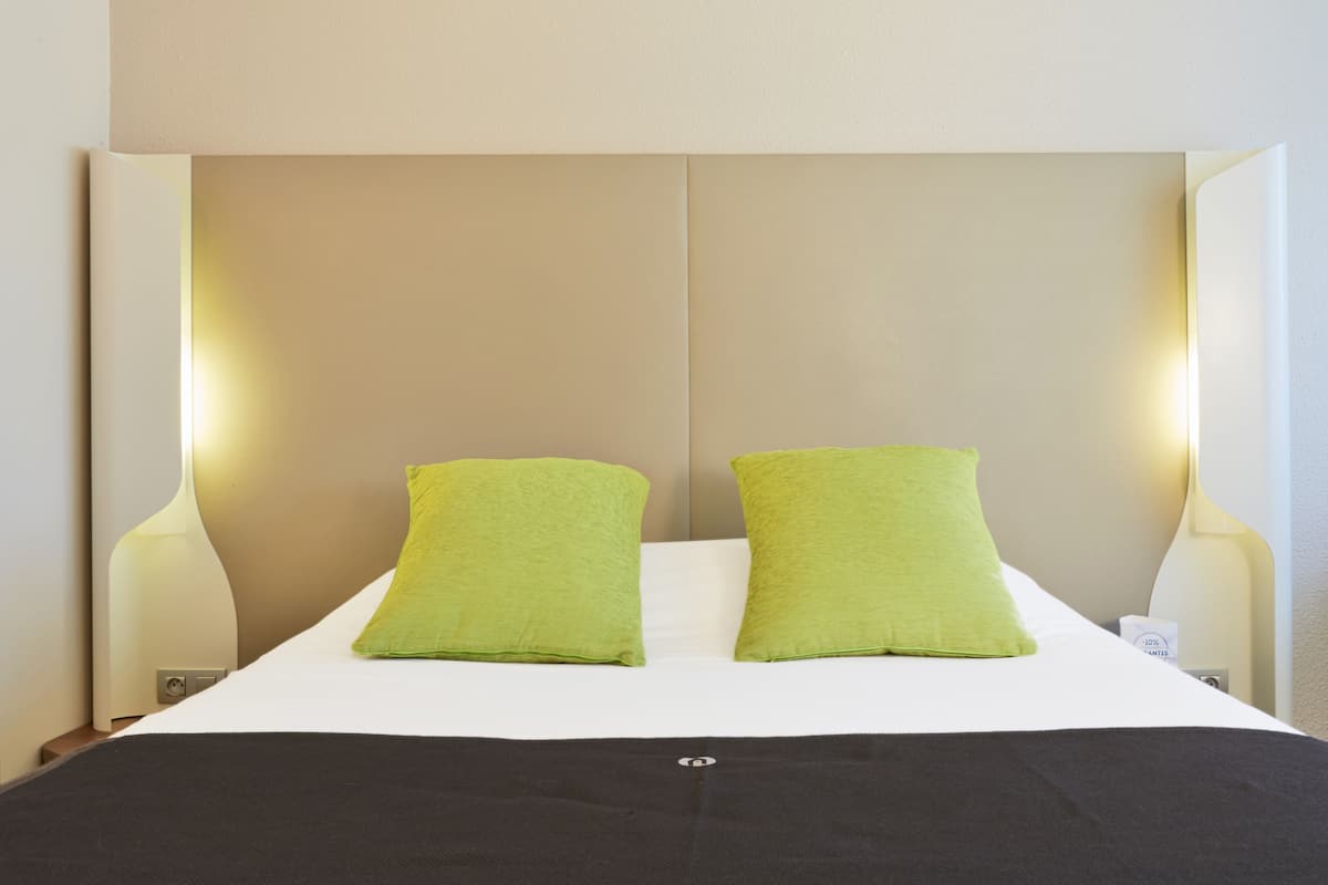 Un lit avec deux oreillers, une table de chevet avec une lampe et un luminaire fixé au mur.