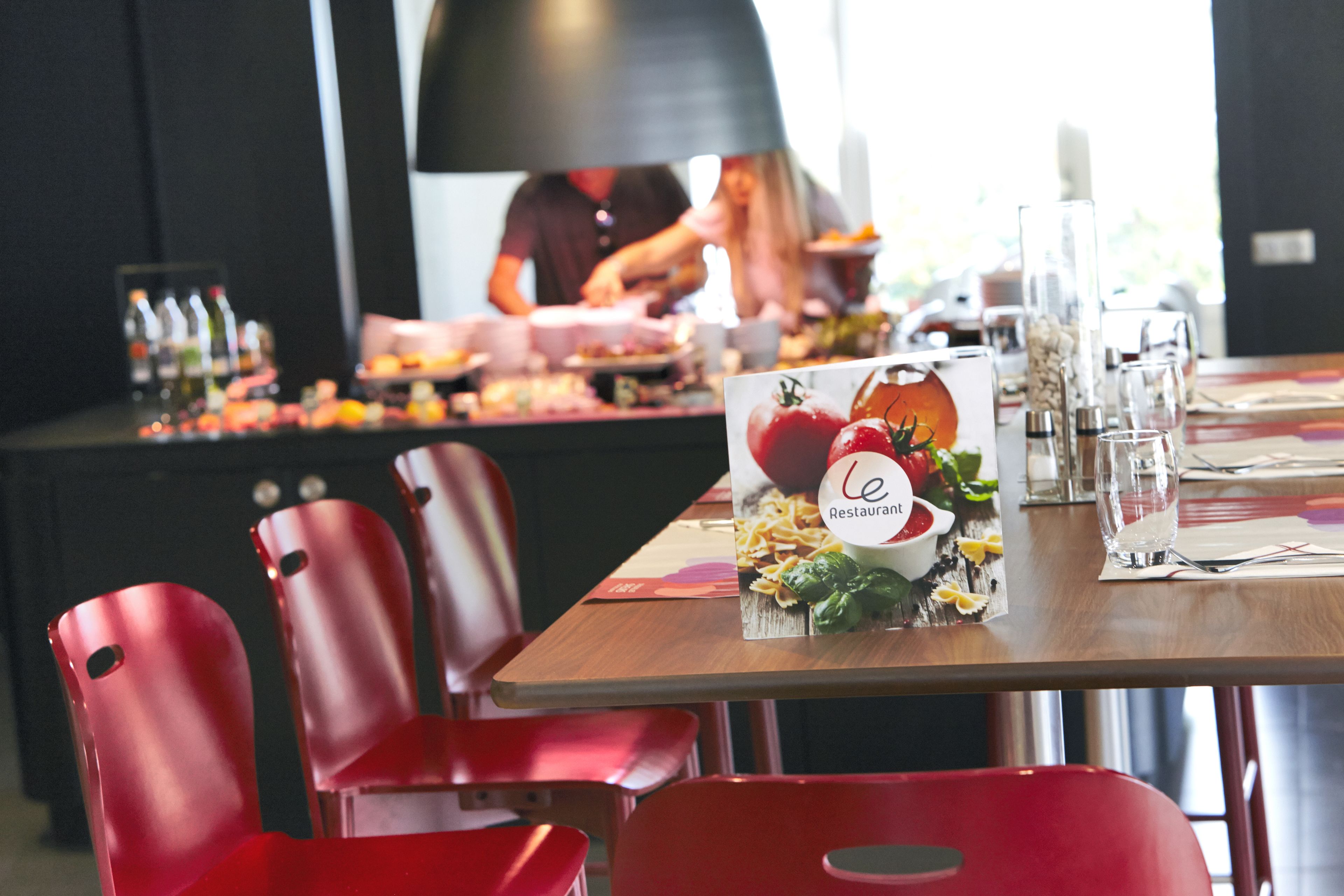A restaurant setting with a wooden table set for dining, red chairs, and a menu stand.