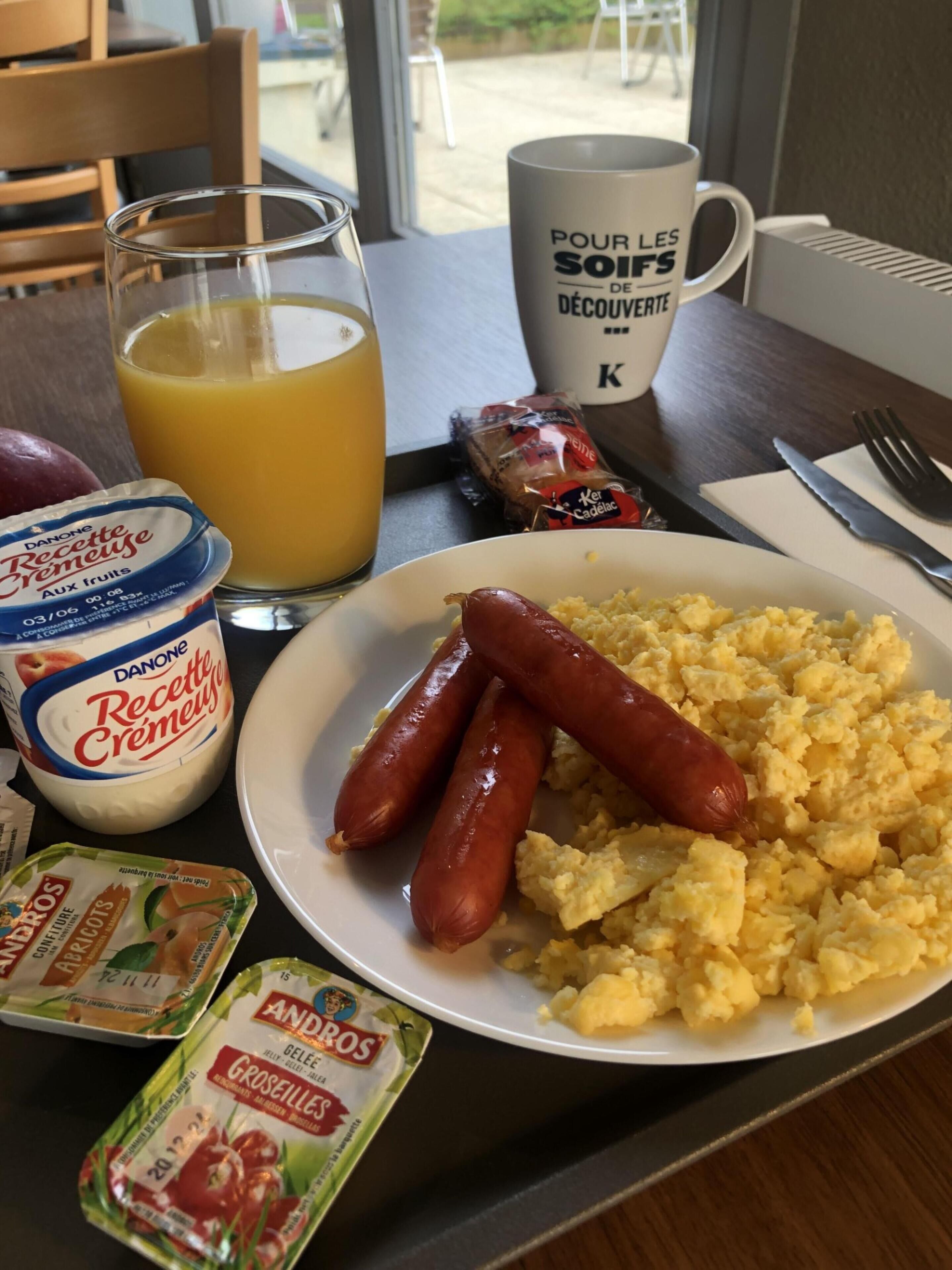A breakfast table with scrambled eggs, sausages, and condiments including Danone yogurt and Andros cheese.