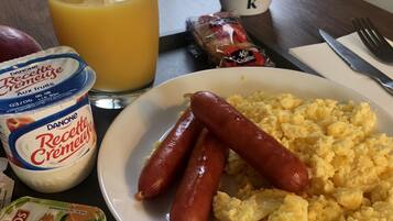 A breakfast table with scrambled eggs, sausages, and condiments including Danone yogurt and Andros cheese.