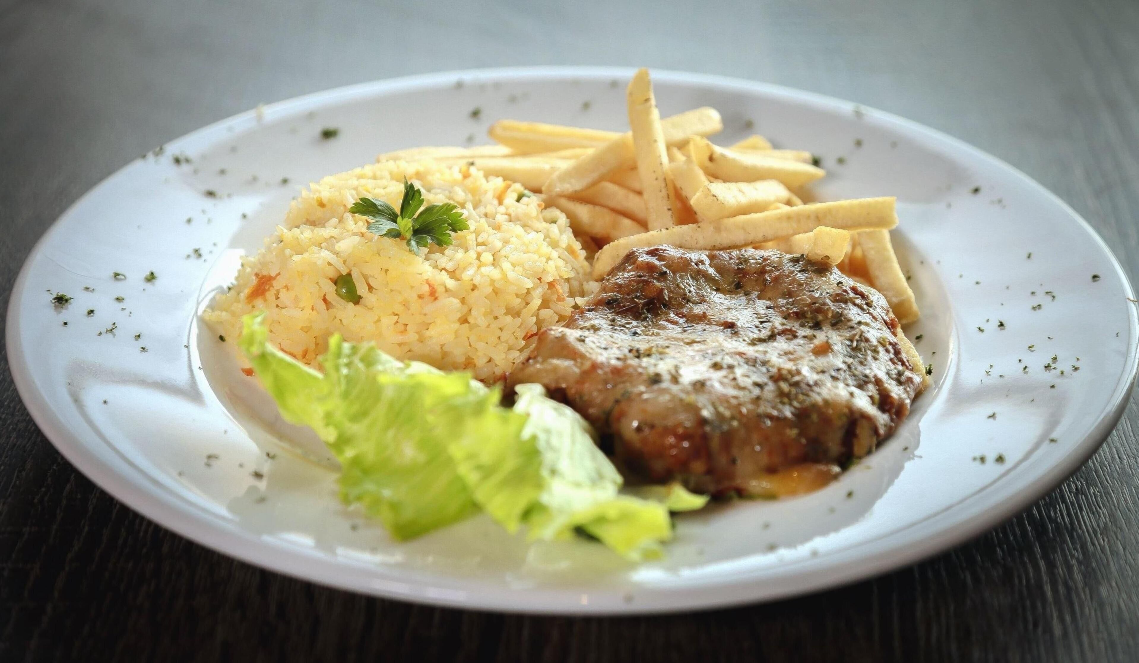 Um prato com arroz, batatas fritas, um prato de carne e uma salada de alface.