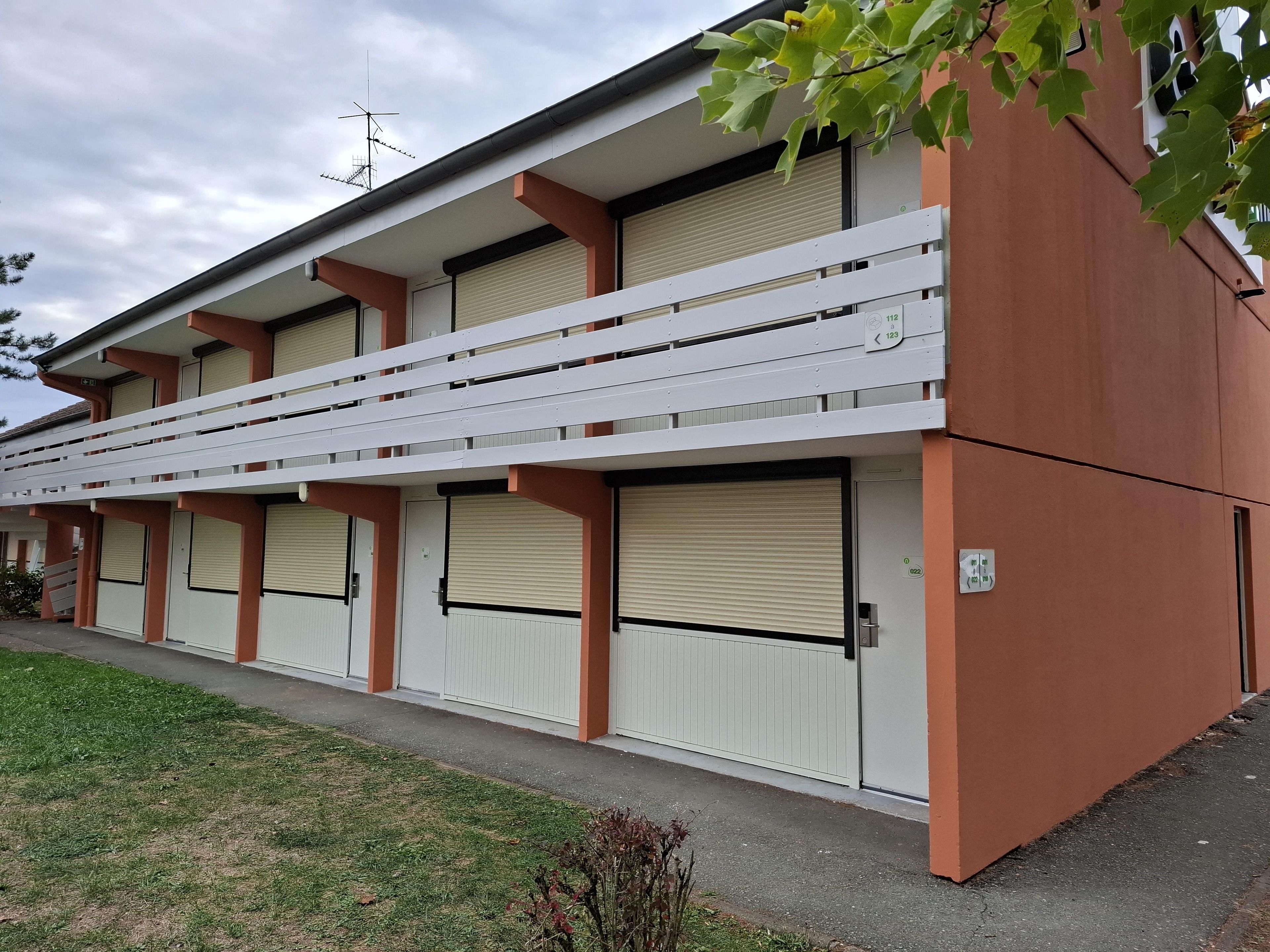 A multi-story building with a flat roof, white balconies, and closed shutters.