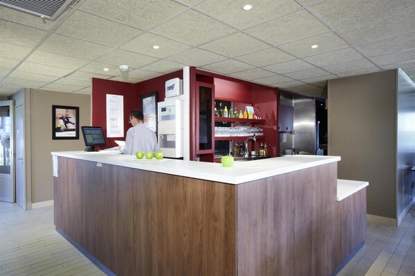 Zona de bar moderna con mostrador de madera, pantalla digital y refrigerador.