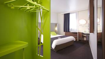 A hotel room with a bed, desk, chair, and a green wall with a hanging rack.