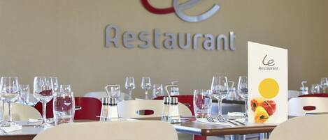 Un interior de restaurante con mesas dispuestas para comer, un atril con la carta y un letrero con el nombre del restaurante.