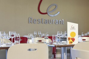 Un interior de restaurante con mesas dispuestas para comer, un atril con la carta y un letrero con el nombre del restaurante.