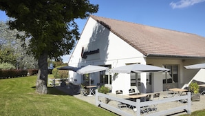 A white building with a tiled roof, outdoor seating area with umbrellas, and a fenced patio.