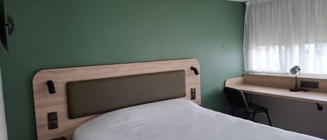 A hotel room with a single bed, a desk, and a chair.