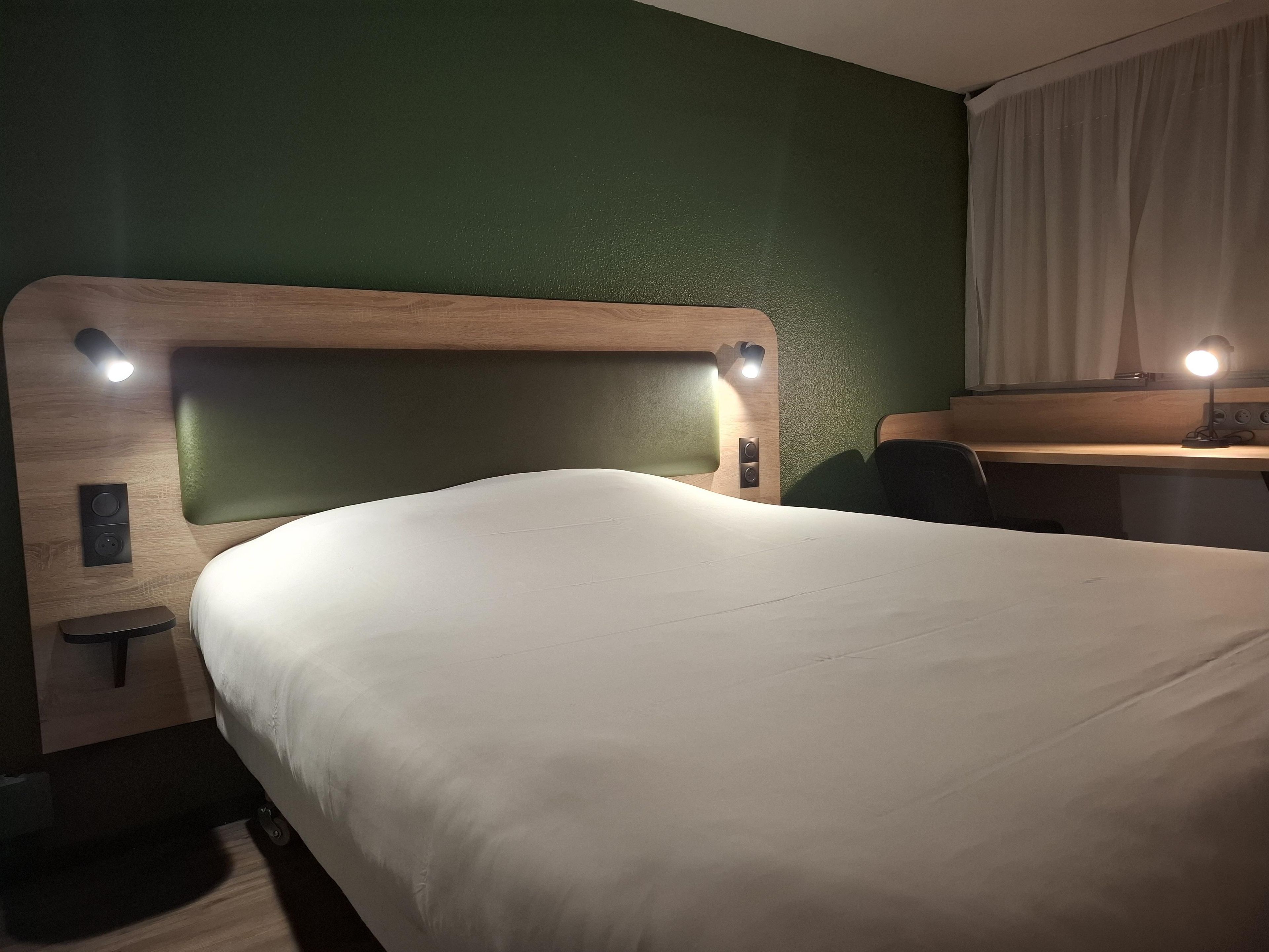 Une chambre d’hôtel comprenant un lit, une table de chevet, une lampe et un petit bureau avec une chaise.