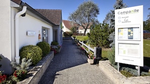 A hotel entrance with a signboard, pathway, and potted plants.