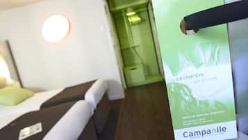 Una habitación de hotel con una cama, una mesita de noche y una pared verde. Hay un cartel en la pared que dice "La chambre est à vous..." y "Merci de faire ma chambre. El espacio es tuyo... Por favor, haz la limpieza.".