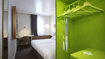 A hotel room with two beds, a desk with a lamp, a chair, a coat rack, and a green wall.