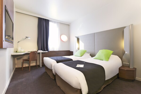 A hotel room with two beds, a desk, a chair, and a nightstand with a lamp.