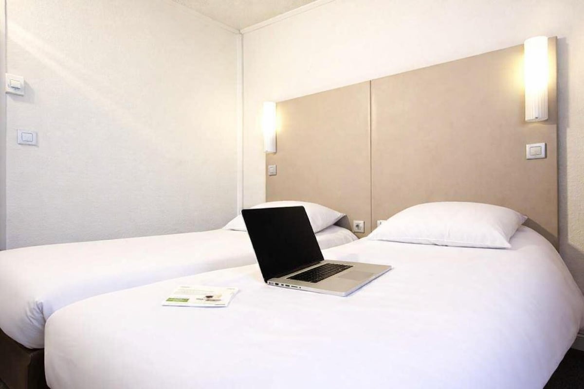 Une chambre d’hôtel avec deux lits, un ordinateur portable posé sur l’un des lits et des lampes fixées au mur.