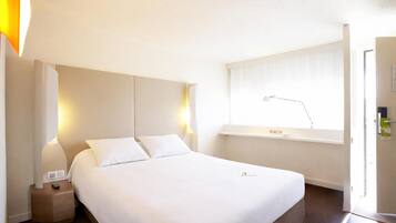 A hotel room with a bed, bedside lamps, a window with curtains, and a nightstand with a remote control.