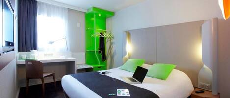 A hotel room with a bed, desk, chair, and a green accent wall.