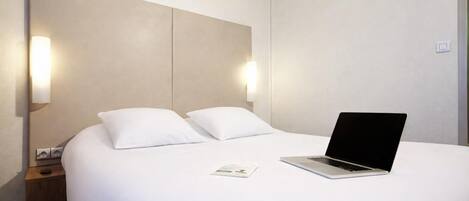 Una habitación de hotel con una cama, una computadora portátil y una mesita de noche.