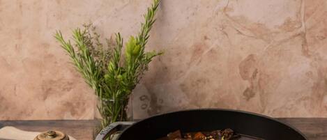 Un recipiente grande de estofado de carne sobre una tabla de madera, con un salero y una ramita de romero al lado.