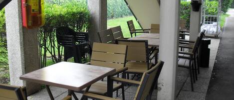 Un patio al aire libre con mesas y sillas, plantas en macetas y un extintor.