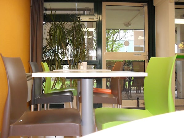 A dining area with a white table and chairs, a potted plant, and a view of the outdoors.