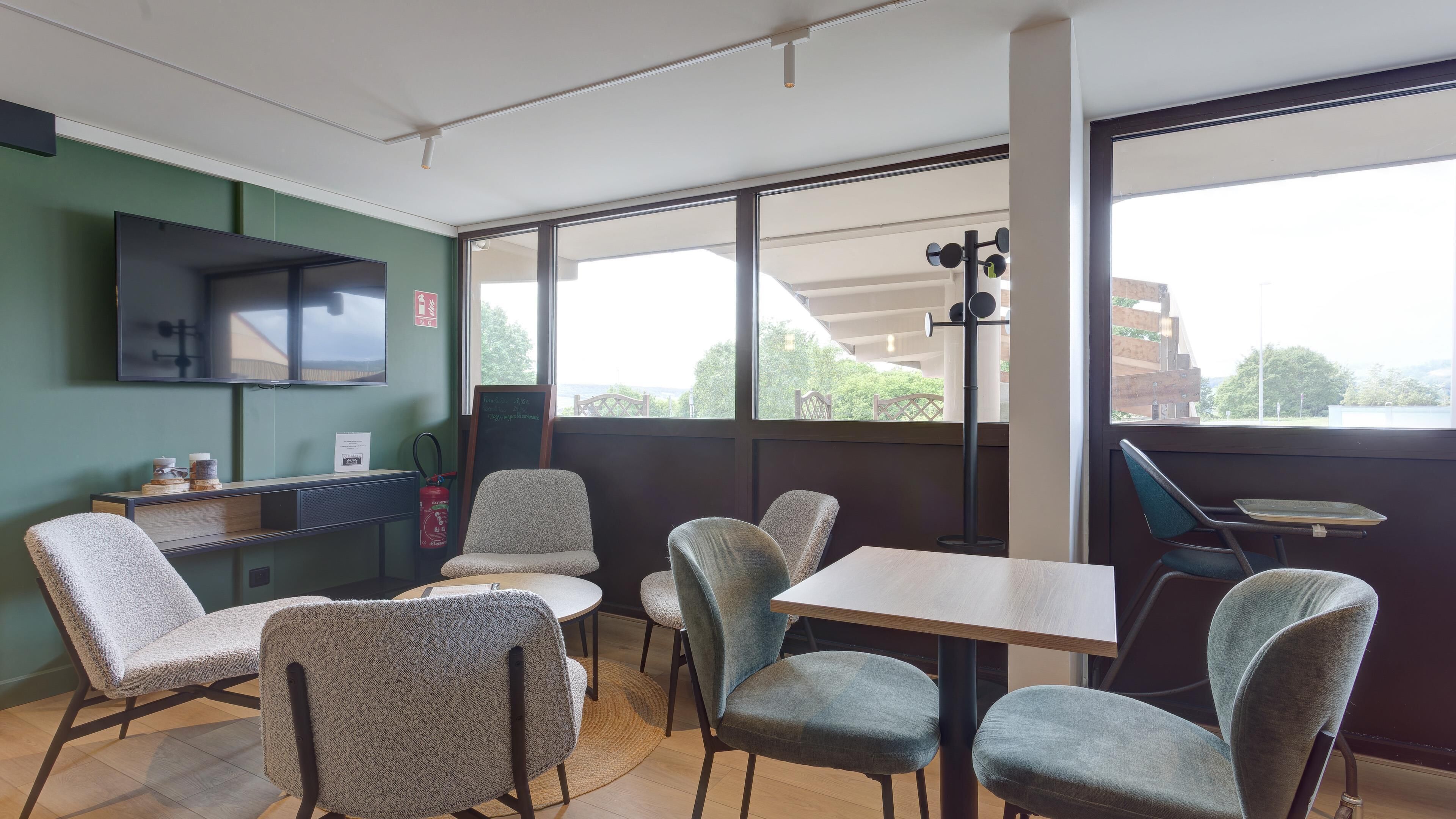 Quarto moderno com uma janela grande, televisão de tela plana, uma mesinha e algumas cadeiras.