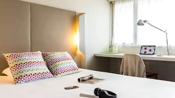 Habitación de hotel con cama, almohadas, escritorio, laptop, lámpara y una silla.