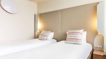 Habitación de hotel con dos camas, cada una con un cojín estampado, una mesita de noche y una lámpara de pared.